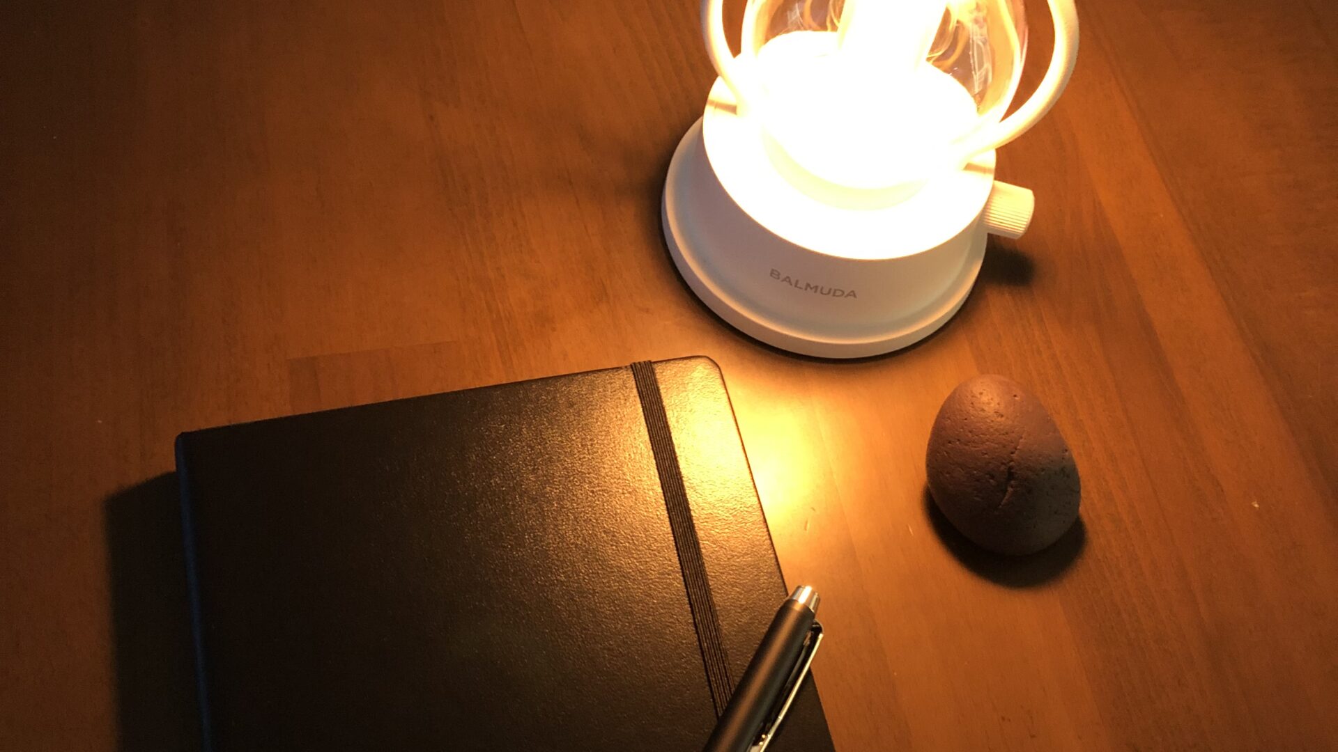 Lamp, stone, and closed journal on a desk in soft light.