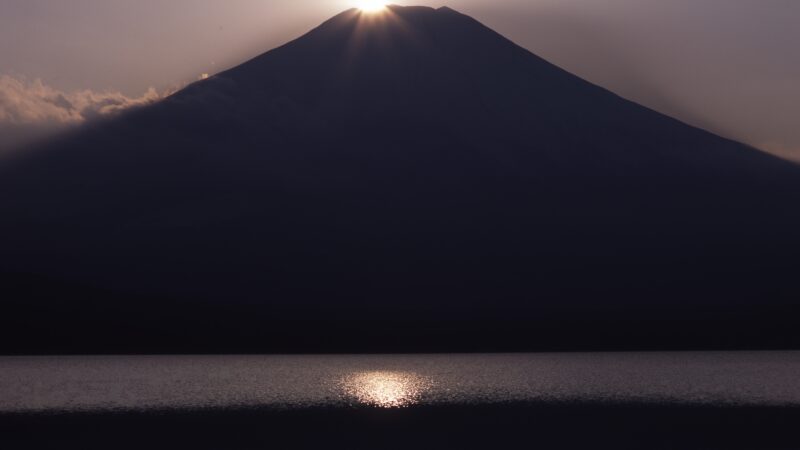 Mt. Fuji reflected on still water at dawn, the sun rising quietly behind — symbolizing clarity, reflection, and alignment.