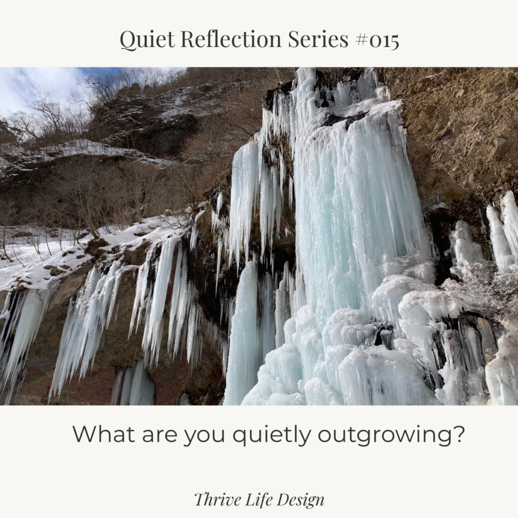 A frozen waterfall captured in winter, ice suspended mid-flow beneath a pale blue sky and soft clouds—movement paused, not gone.