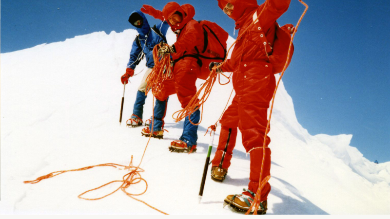 Mountain climbers walking in a line along a snowy slope, linked by a rope.